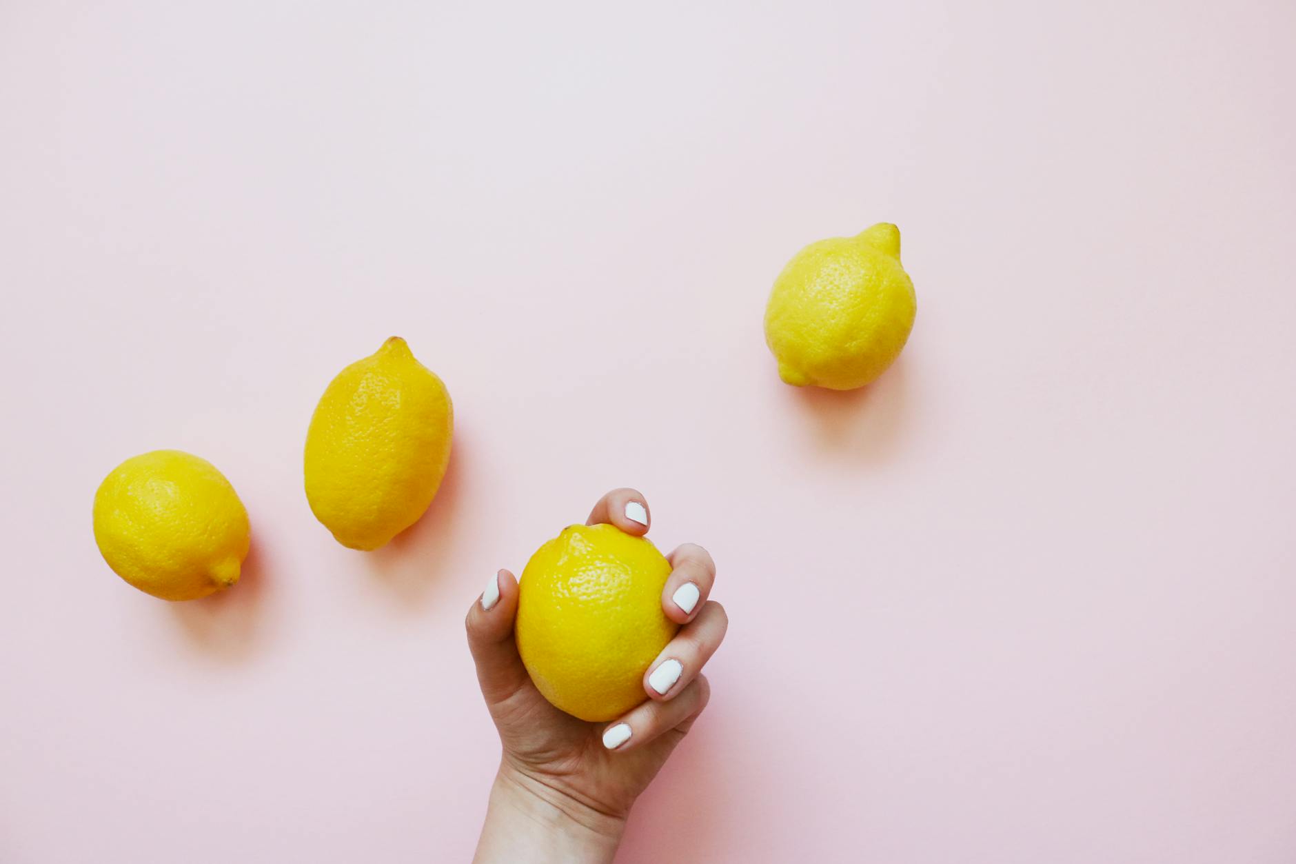 Hand holding a fresh lemon on soft pink background surrounded by additional lemons