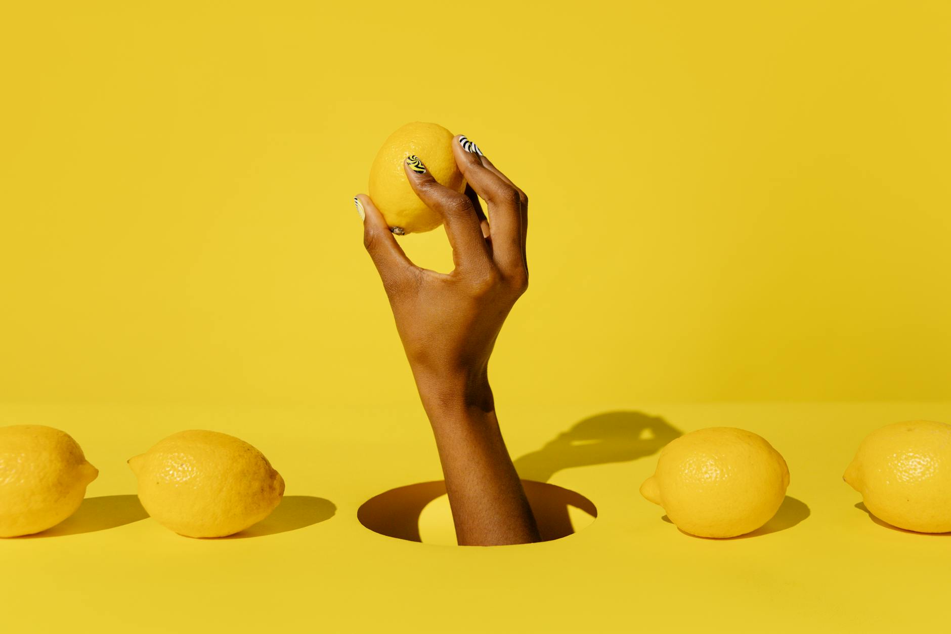 Hand holding a fresh lemon against a vivid yellow background, symbolizing the lemon vibrator's citrusy design