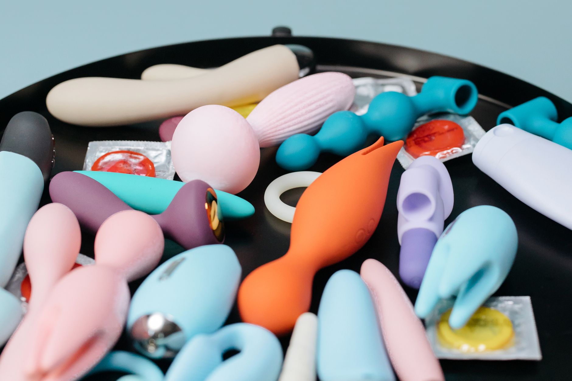 Colorful vibrators with flowers displayed in a vibrant holographic gift bag on a bold yellow background