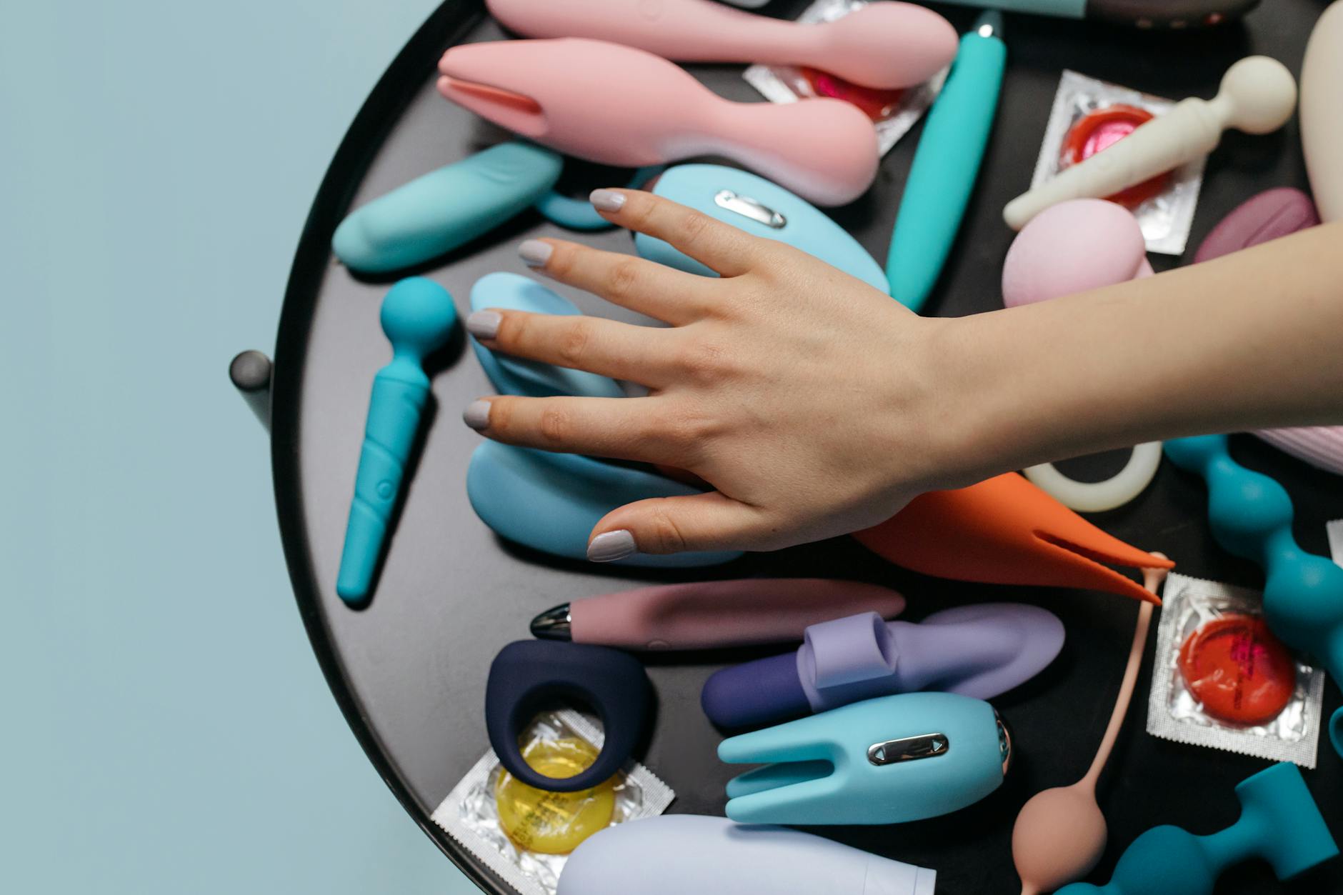 A hand reaching over a variety of colorful lemon and berry clitoral vibrators arranged on a table