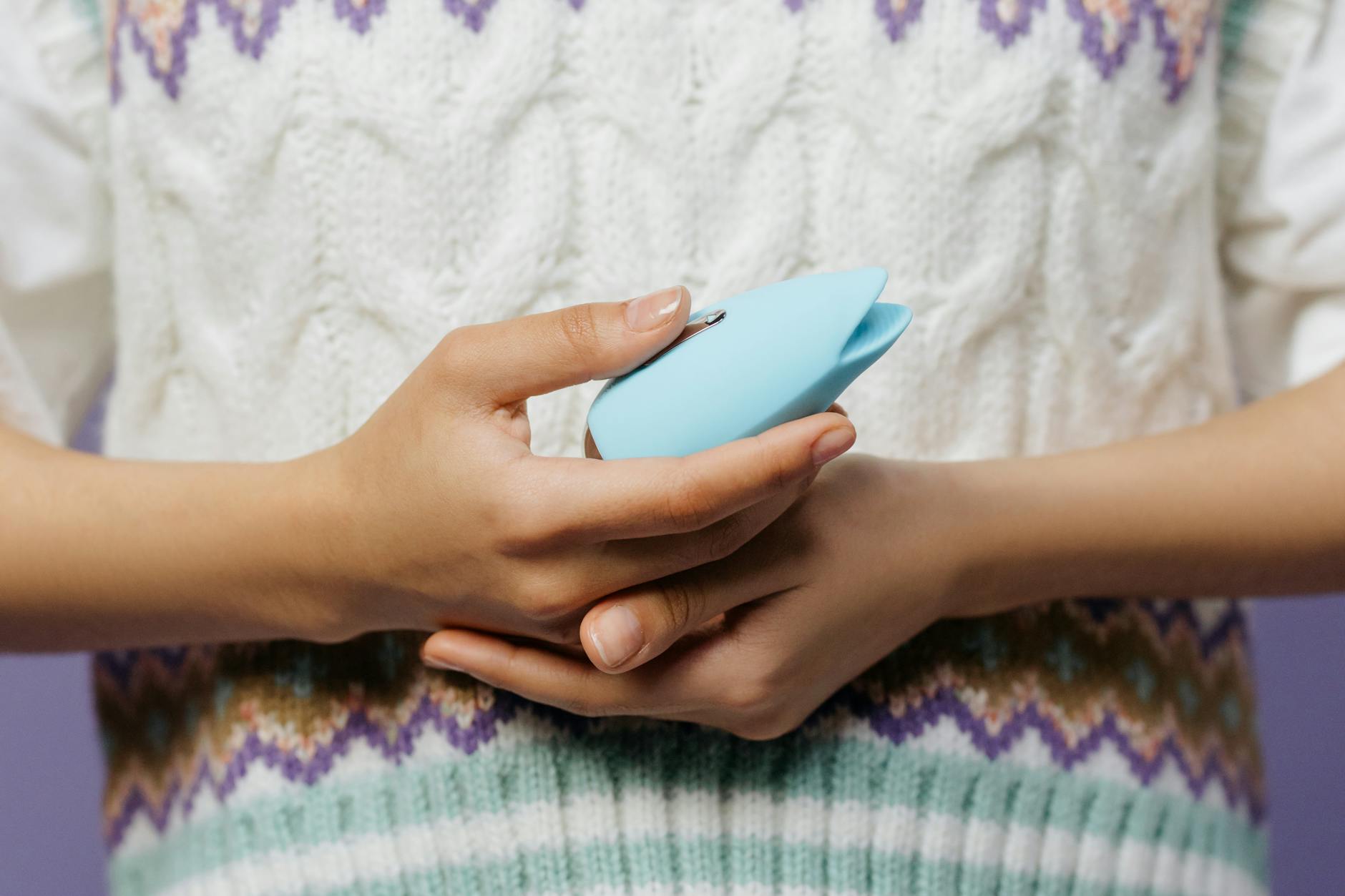 A close-up of hands holding a blue personal massager against a knitted sweater.